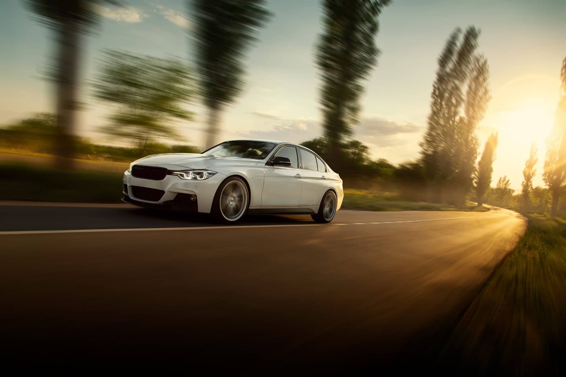 Bílé auto rychle projíždějící krajinou při západu slunce