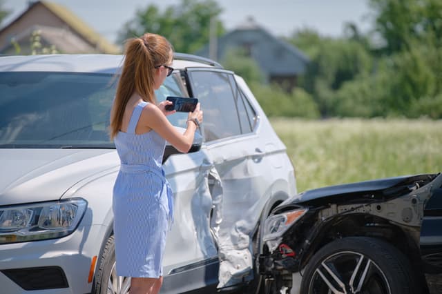 Žena mobilem dokumentuje poškozený vůz po dopravní nehodě.