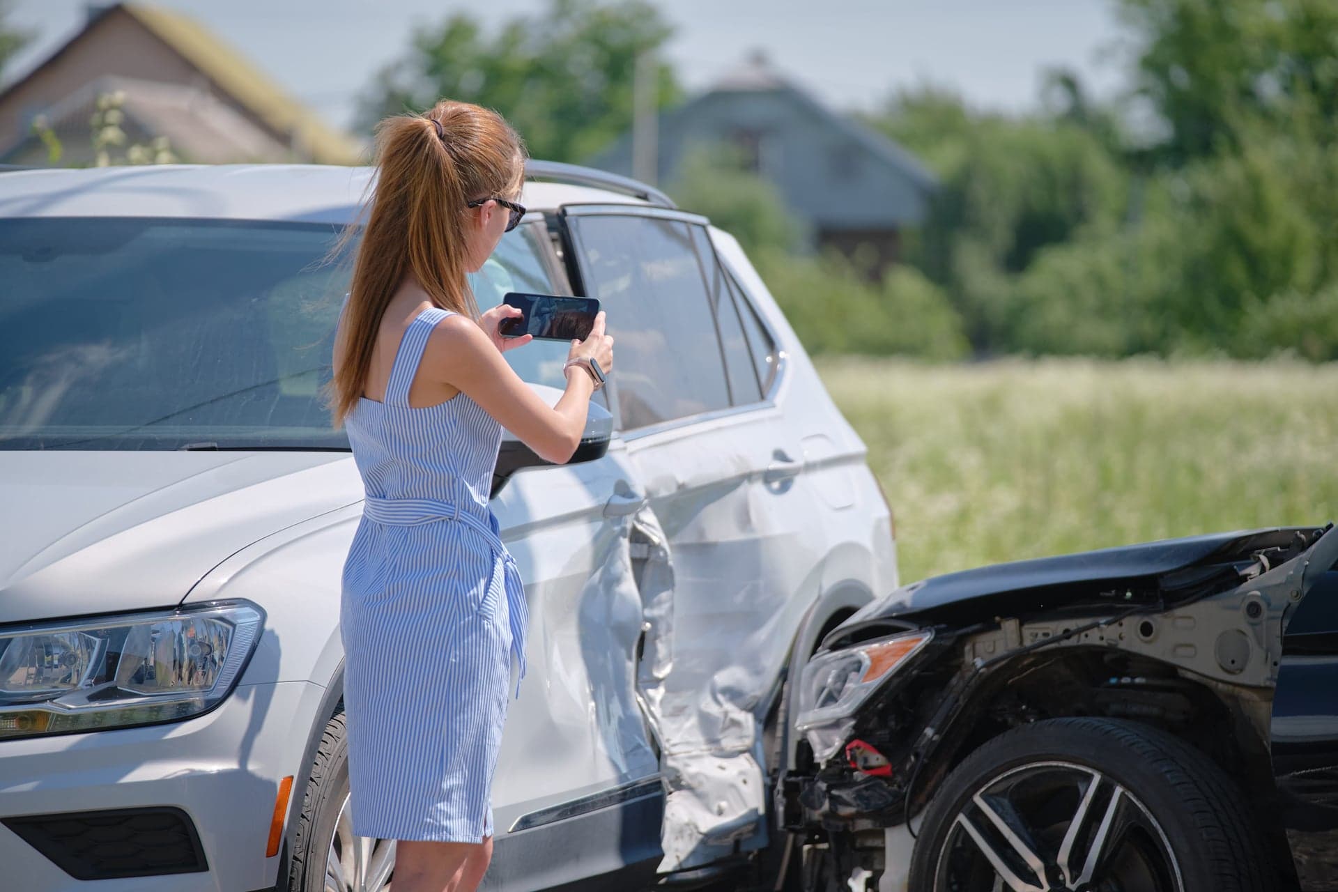 Žena mobilem dokumentuje poškozený vůz po dopravní nehodě.