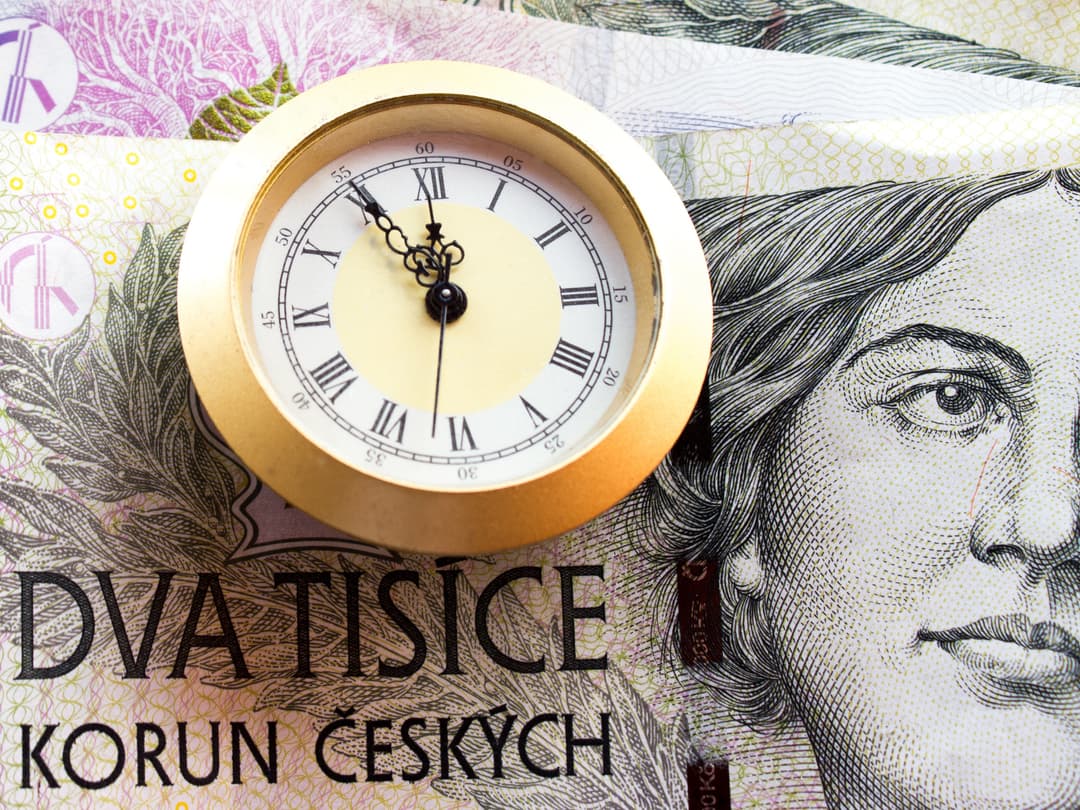 Hodiny položené na českých bankovkách dvoutisíc korun, symbolizující čas a peníze